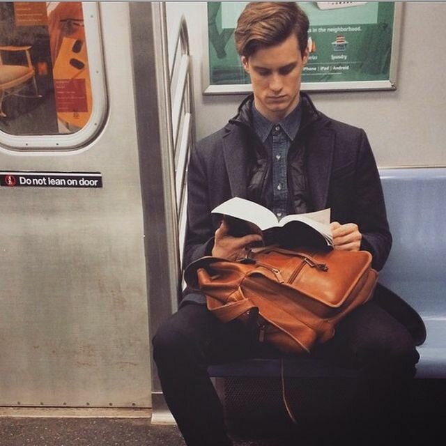 На фотографии: Молодой человек читает книгу в метро